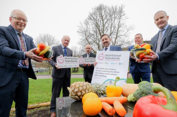 Six food and health officials show a report with a table of fresh fruit in the foreground